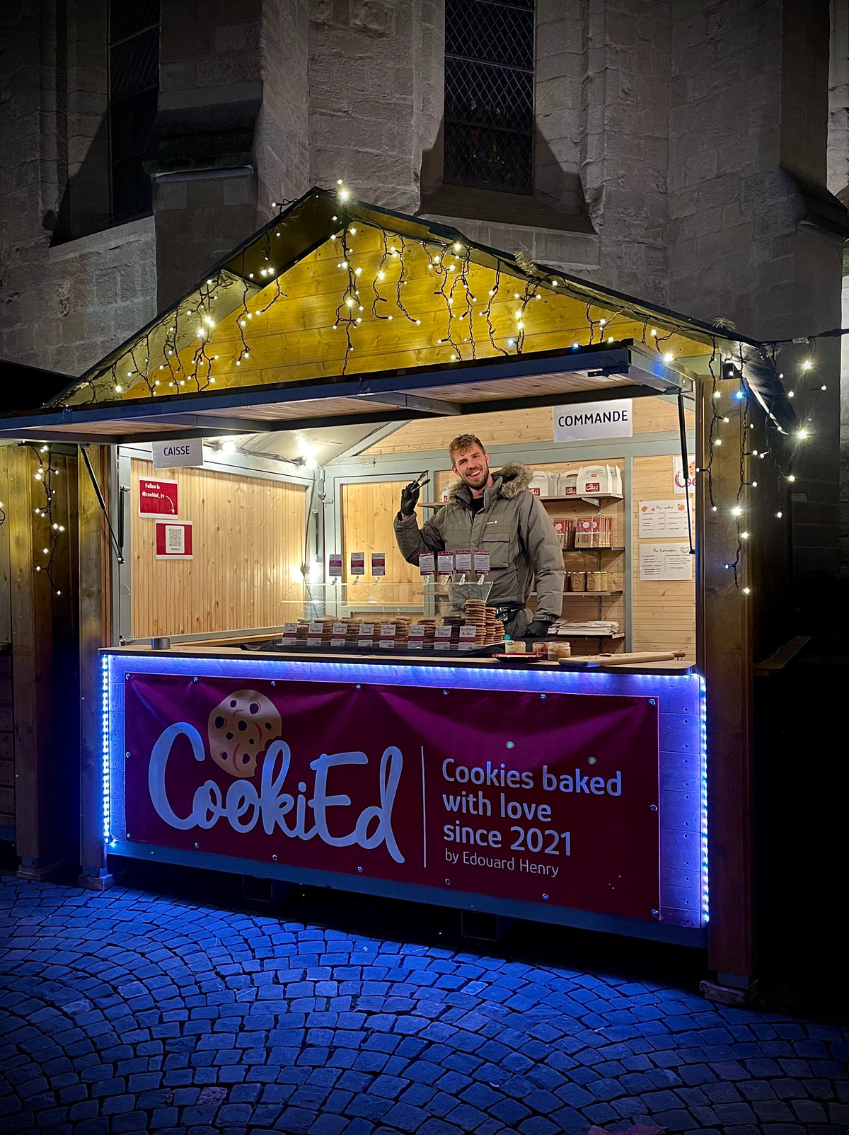 Edouard Henry dans le chalet illuminé de CookiEd à un marché de Noël, cookies en vitrine